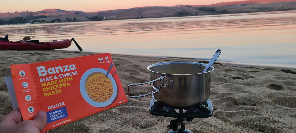 Dinner cooking on camp stove at the beach as the sun sets over the bay