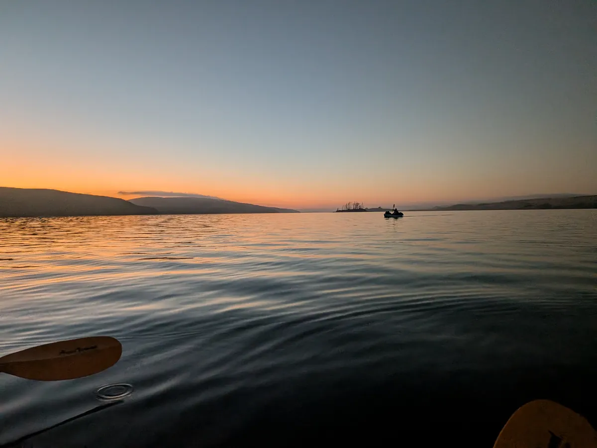 Looking across the bay at dusk from the cockpit, paddle blades in the foreground