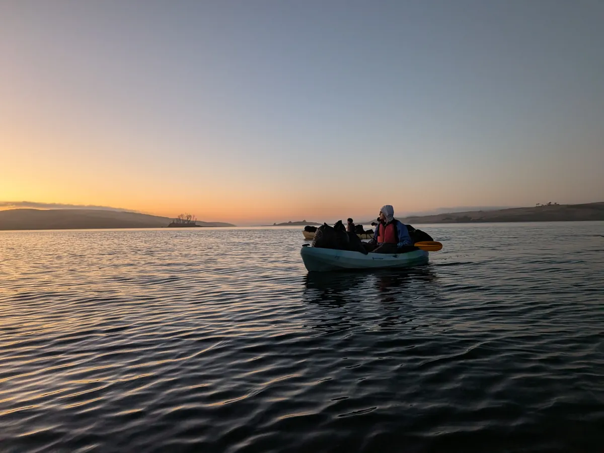 A loaded kayak on calm water at sunset, Hog Island in the distance